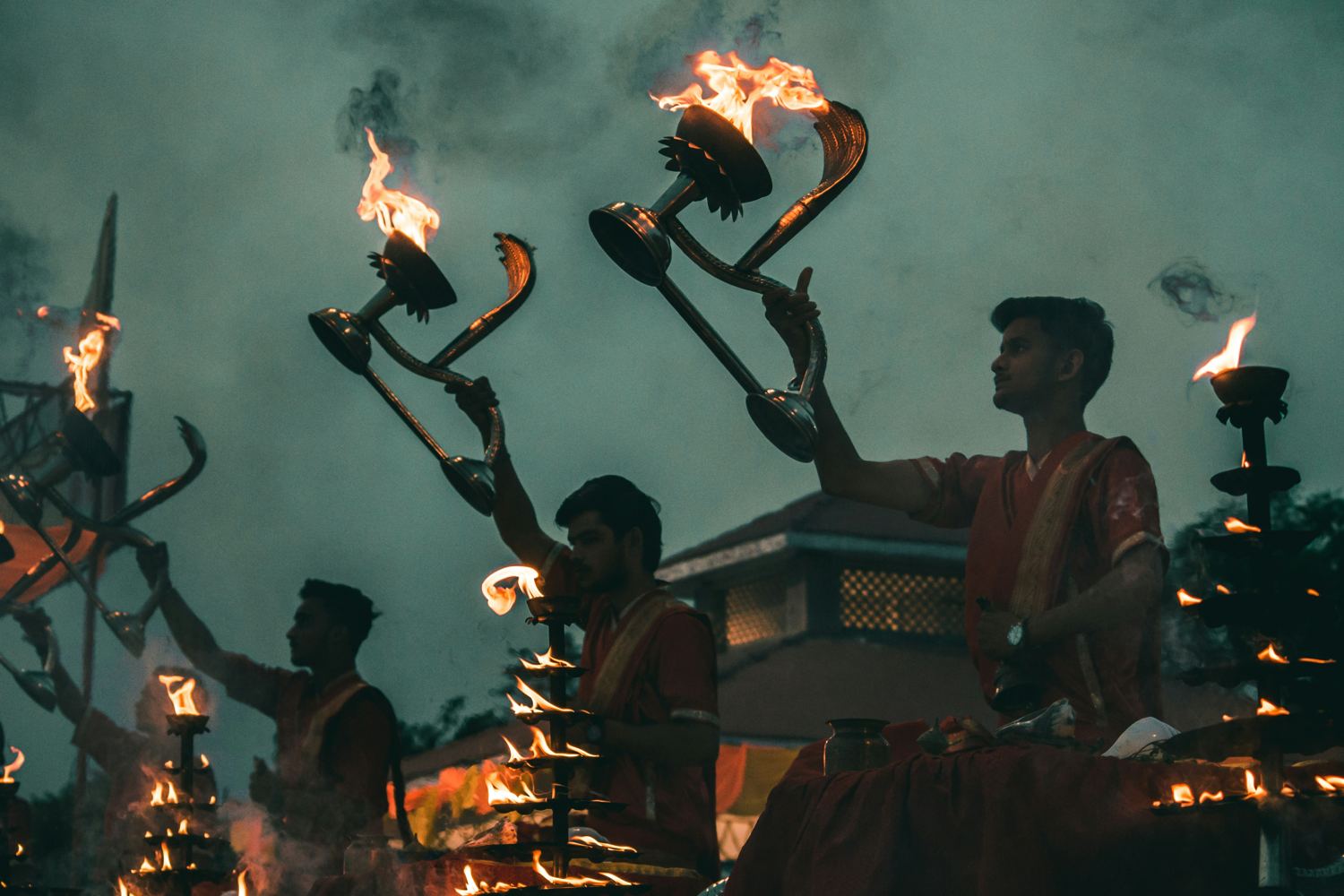 Priests on the ghats holding flaming aarti lamps against a dusk sky